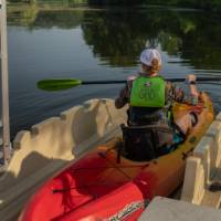 woman, photo taken over the shoulder, in a single kayak using an accessible launch to get onto the water